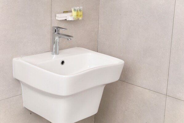 A white pedestal sink with a modern faucet, a small shelf above holding toiletries, and a tiled wall. - Wedyan City (Madinah)