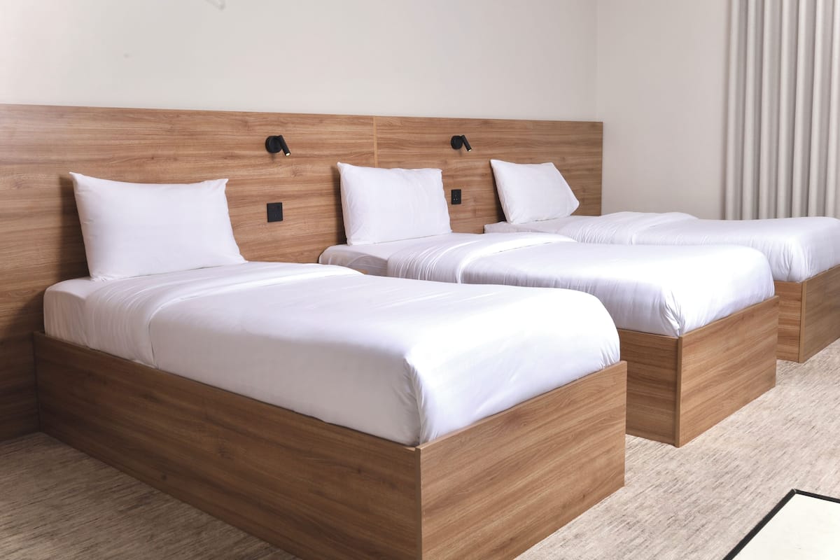 A hotel room with three wooden beds, each with white bedding and headboards.