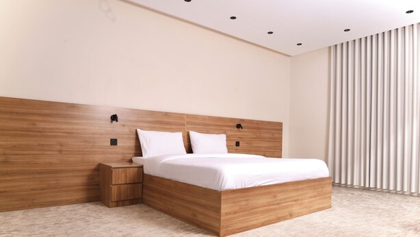 Een moderne slaapkamer met een houten hoofdbord, een nachtkastje van hout en een groot bed met wit beddengoed.