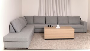 Een moderne woonkamer met een grijze modulaire bank, een houten salontafel en een lichtkleurig vloerkleed.