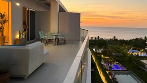 Un balcon avec vue sur la mer au coucher du soleil, des sièges en plein air et un espace piscine bien éclairé.
