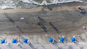 Une vue aérienne d’une plage avec des personnes, des parasols et des chaises de plage.