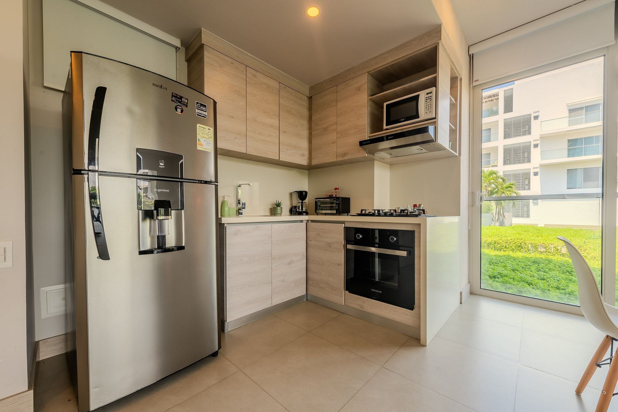 A modern kitchen with a stainless steel refrigerator, built-in microwave, oven, and a large window offering a view of the outside.