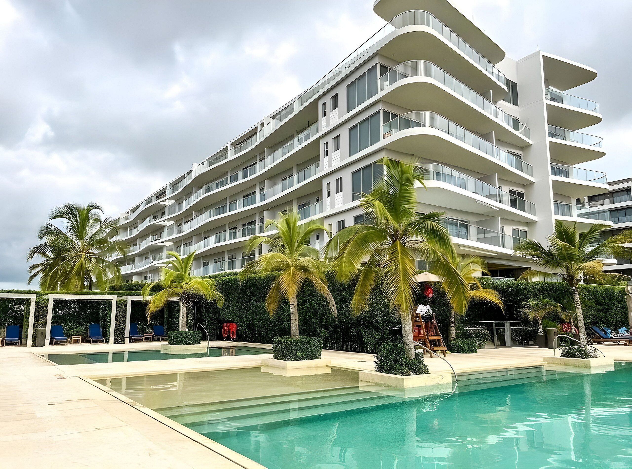 A modern hotel with multiple balconies, a swimming pool, and palm trees.