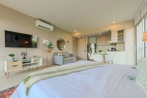 A modern bedroom with a large bed, a TV mounted on the wall, a desk, and a kitchenette area. - Morros IO by ID (Cartagena)