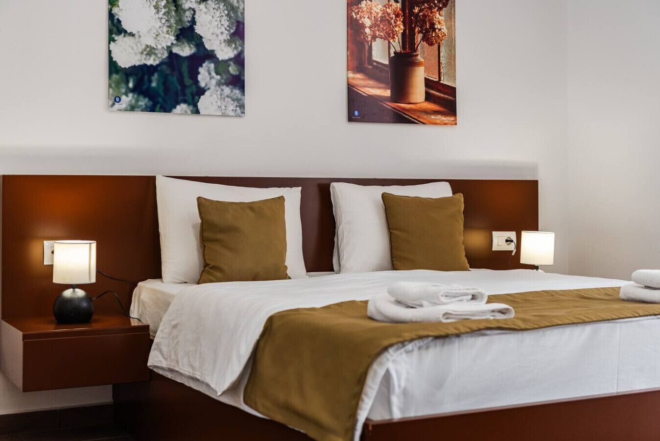 Une chambre d’hôtel avec un grand lit, deux tables de chevet, une petite table, une lampe et un tableau au mur.