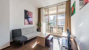 Un soggiorno moderno con un divano grigio, un tavolino, una televisione e una grande finestra con vista sulla città.
