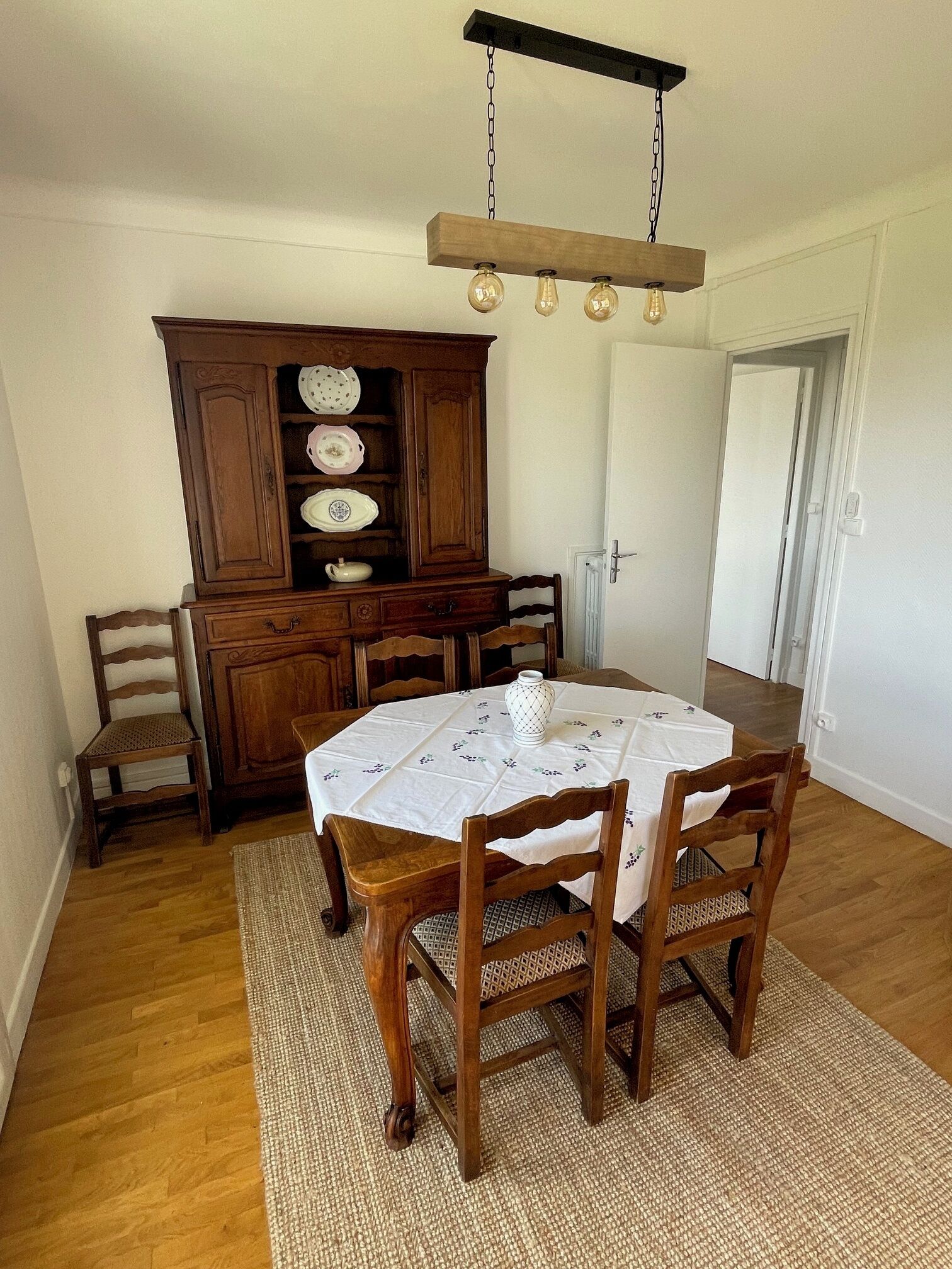 A dining area with a wooden table and chairs, a cabinet with dishes, and a hanging light fixture.