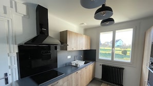 A modern kitchen with black appliances, wooden cabinets, and a large window offering a view of the outdoors.