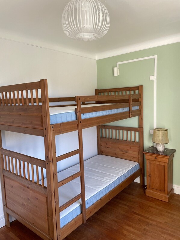 Una cama litera con estructura de madera y una mesita de noche con lámpara.