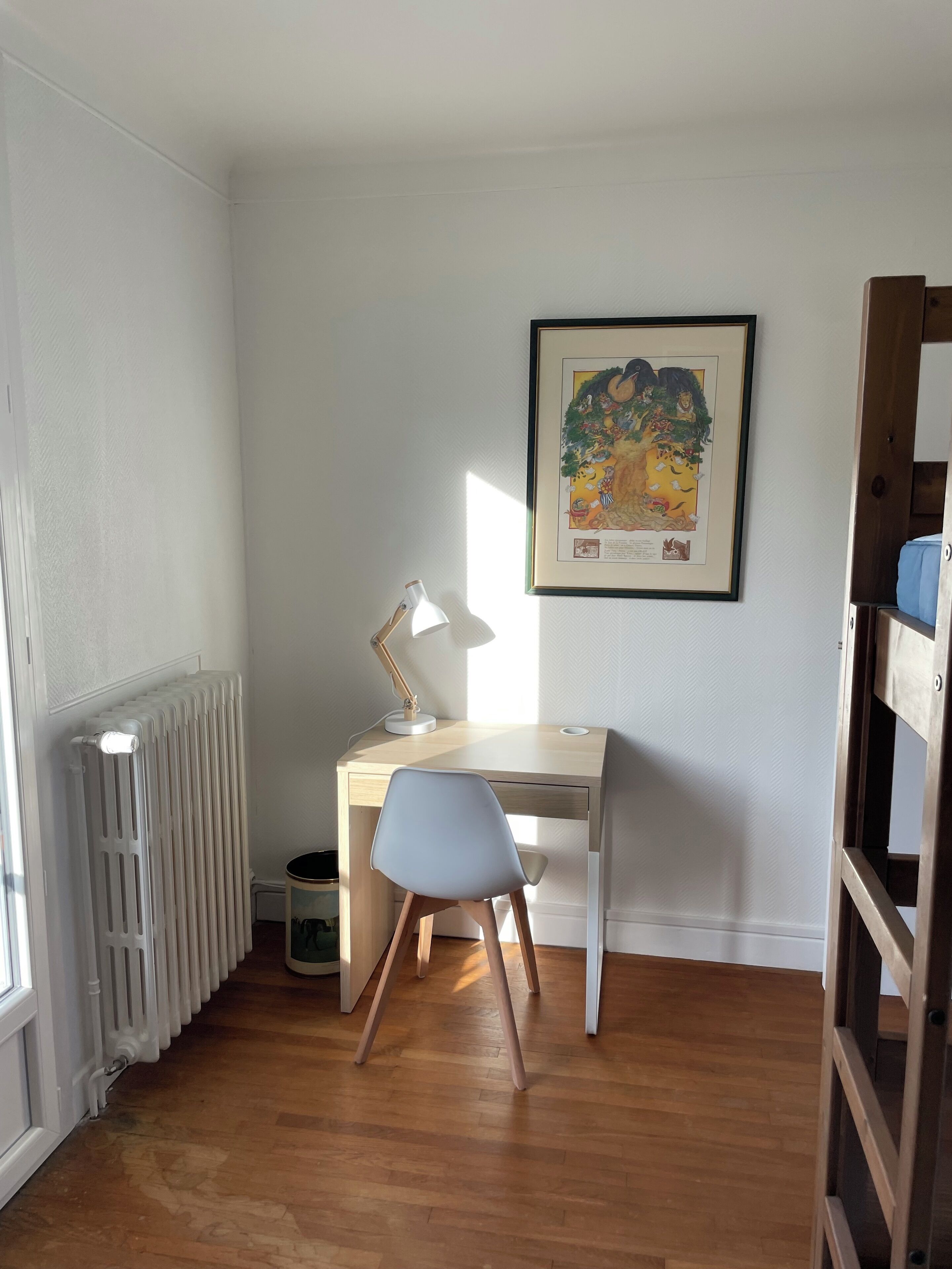 Una habitación con un escritorio de madera, una silla blanca, un radiador y un cuadro en la pared.