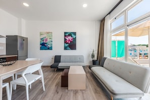 A modern living room with a sofa, a dining table with chairs, and artwork on the wall.