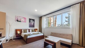 A modern hotel room with a large bed, a sofa, a coffee table, and a view of the outside. - Modern Studio by the Beach - Orkidea by PikHost (Gjiri i Lalzit)