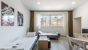 Una habitación moderna y bien iluminada con dos camas individuales, un sofá, una mesita y un televisor.
