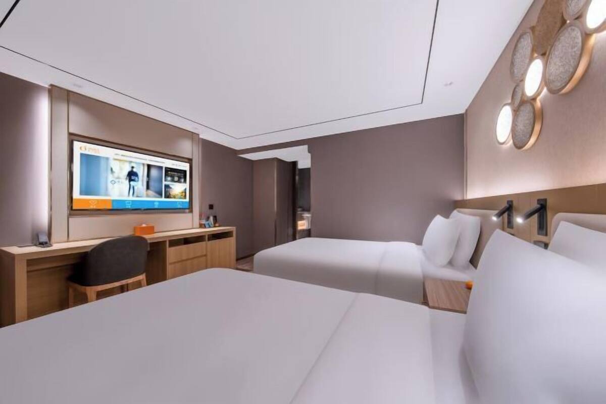 Quarto de hotel moderno com uma cama grande, uma escrivaninha e uma televisão exibindo um site.