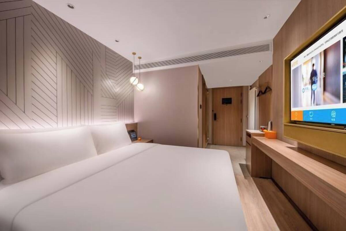 Quarto de hotel moderno com uma cama grande, uma parede de destaque em madeira, uma televisão e uma mesa com um computador.