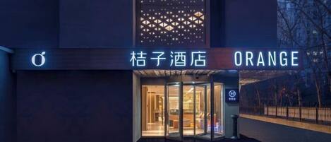 A hotel entrance with a revolving door, a sign with the name "Orange" and Chinese characters, and a modern facade with geometric patterns.