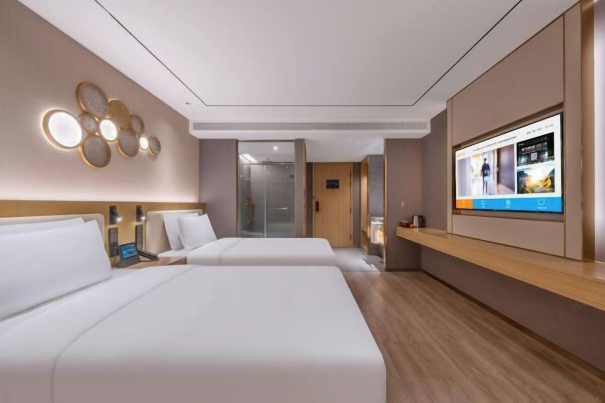 Quarto de hotel moderno com duas camas, televisão na parede e piso de madeira.