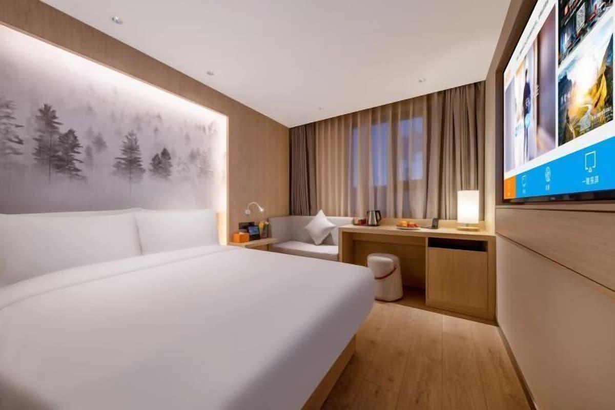 Une chambre d’hôtel avec un grand lit, un bureau, une chaise, une télévision et un mur orné d’une fresque sur le thème de la nature.