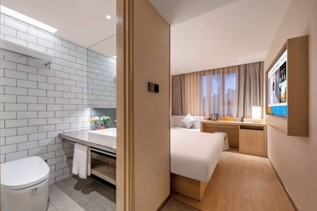 Quarto de hotel com banheiro, uma cama, escrivaninha e televisão.