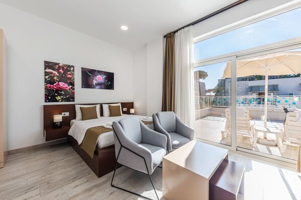 Habitación de hotel con cama, dos sillas, escritorio y balcón con mobiliario exterior.