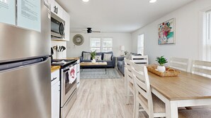 A modern kitchen with stainless steel appliances, a dining area with a wooden table and white chairs, and a living room with a sofa and a coffee table. - Charming duplex with balcony,  W/D, central AC & steps to beach (Murrells Inlet)