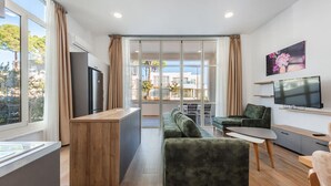 Uma sala de estar moderna com sofá, mesa de centro, televisão e área de cozinha com geladeira e bancada de madeira.