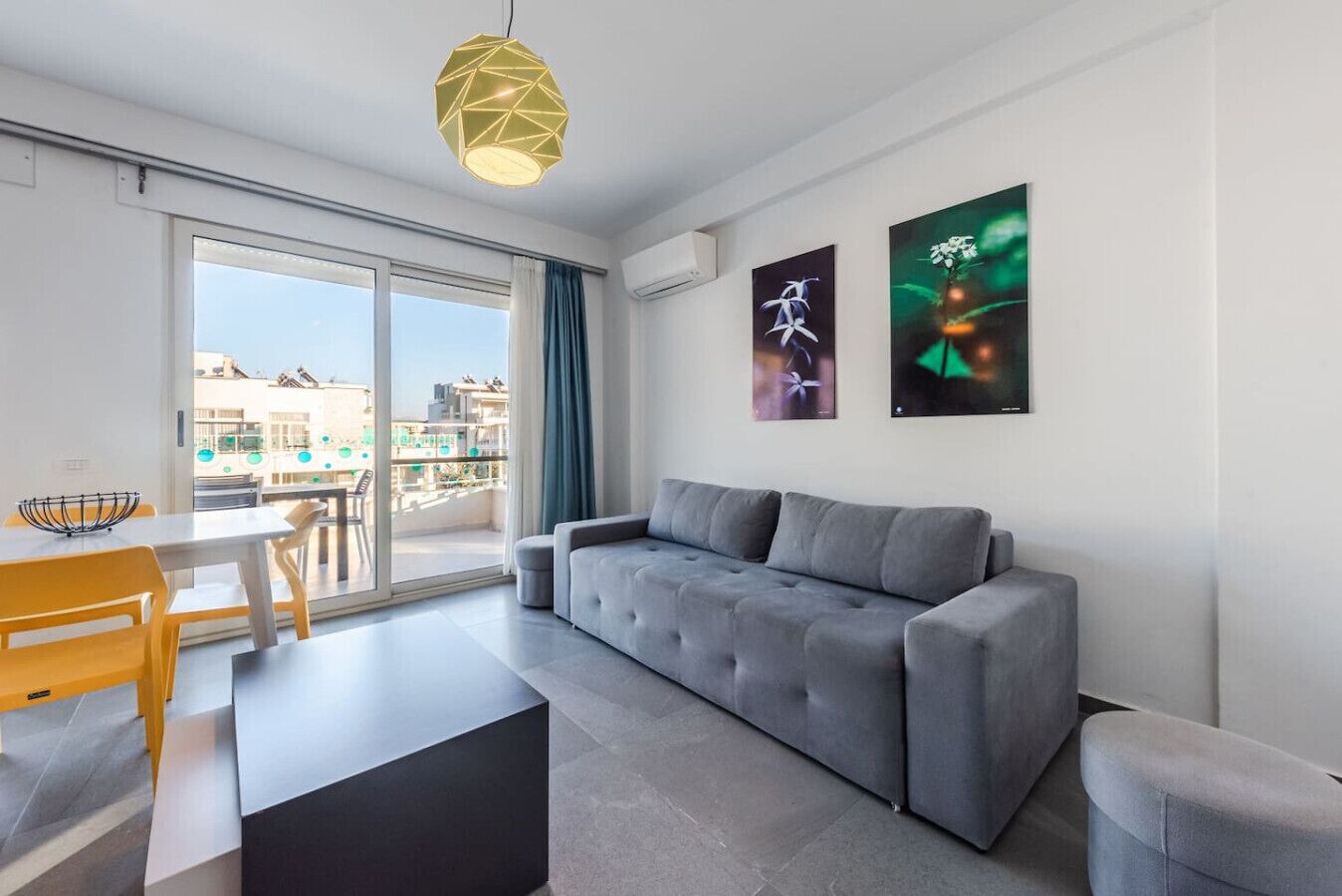 Una sala de estar moderna con un sofá gris, una mesa de comedor con sillas amarillas y un amplio ventanal con vistas a la ciudad.