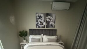 A neatly made bed with white bedding, a grey headboard, and two wall-mounted flower paintings. - Modern, safe and very clean self catering apartment . (Gaborone)