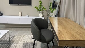A modern room with a wooden dining table, a black upholstered chair, a white console, a flat-screen TV mounted on the wall, and a potted plant. - Modern, safe and very clean self catering apartment . (Gaborone)