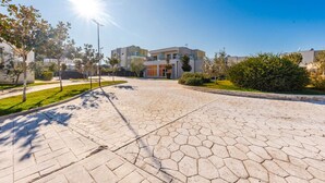 A paved walkway leading to a modern building with a glass facade, surrounded by greenery and trees. - Tranquil Apartment with pool access - Manjola by PikHost (Gjiri i Lalzit)