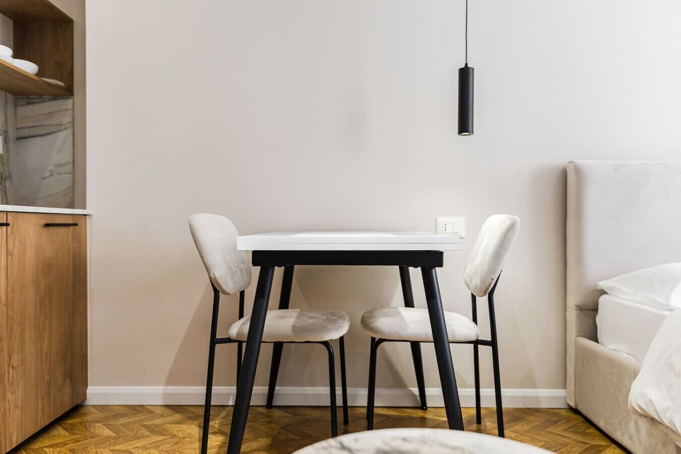 A small, modern room with a white table and two chairs, a wooden cabinet, and a hanging light fixture.