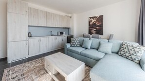 A modern living room with a light blue sofa, a coffee table, and a kitchen area with white cabinets and a microwave. - Serene Haven Talea by PikHost (Tale)