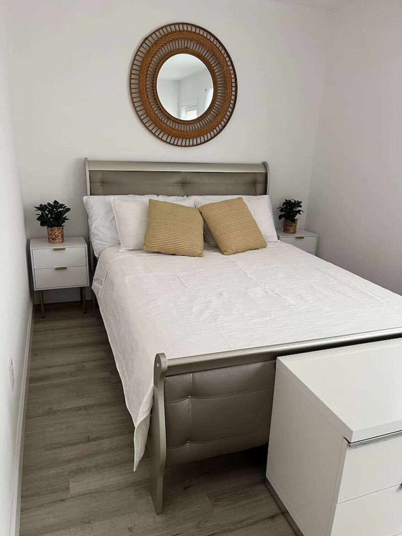 Une chambre à coucher bien rangée, avec un lit, deux tables de chevet, une commode, un miroir et une coiffeuse.