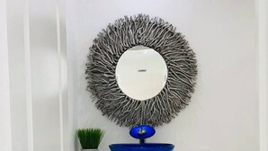 A white cabinet with two doors, a blue bowl on top, and a round mirror with a textured frame.