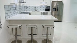 A modern kitchen with a white island, stainless steel appliances, and a tiled backsplash.