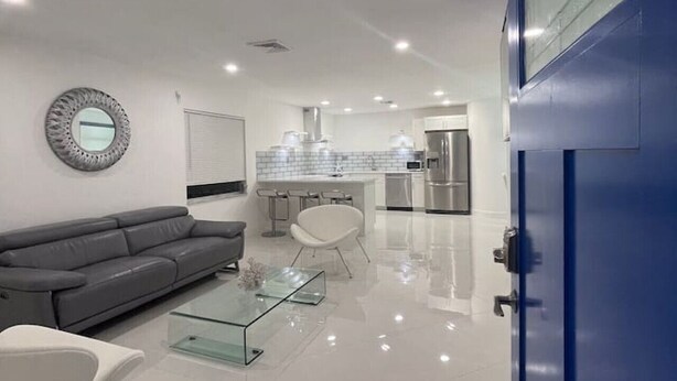 A modern living room with a glass coffee table, a grey sofa, and a white chair.