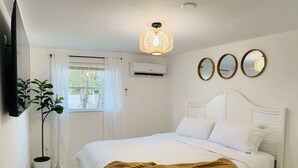 A bedroom with a bed, a potted plant, a wall-mounted air conditioner, and a ceiling light fixture.