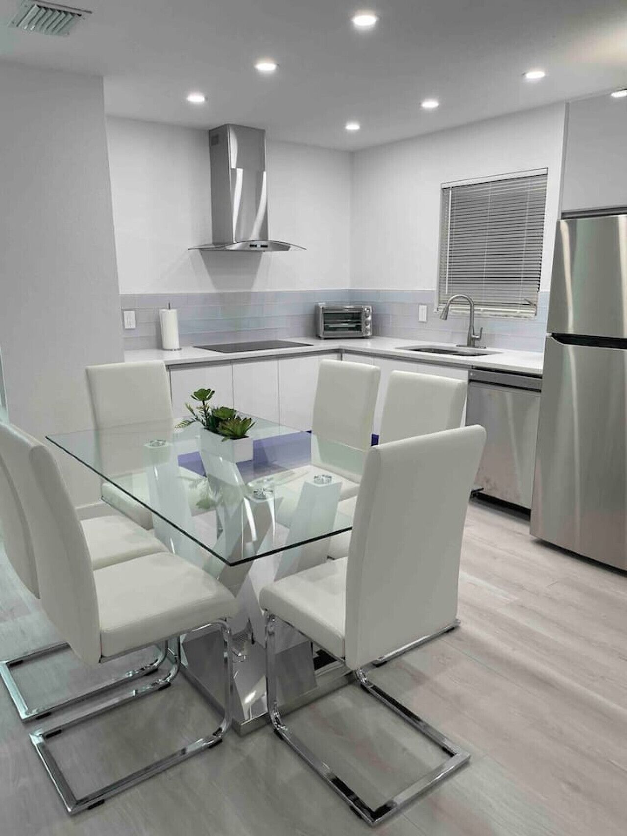 Una cocina moderna con armarios blancos, una campana extractora de acero inoxidable, horno integrado y refrigerador.