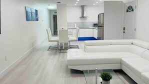 A modern living room with a white sectional sofa, a glass coffee table, and a dining area with white chairs.