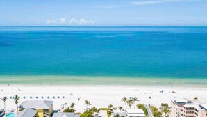 A beach view with a clear sky, a sandy beach, and a few buildings in the foreground. - Beautiful apartment two mins away from the beach! (Fort Myers Beach)