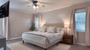 Een slaapkamer met een bed, nachtkastjes, een plafondventilator en een aan de muur bevestigde televisie.