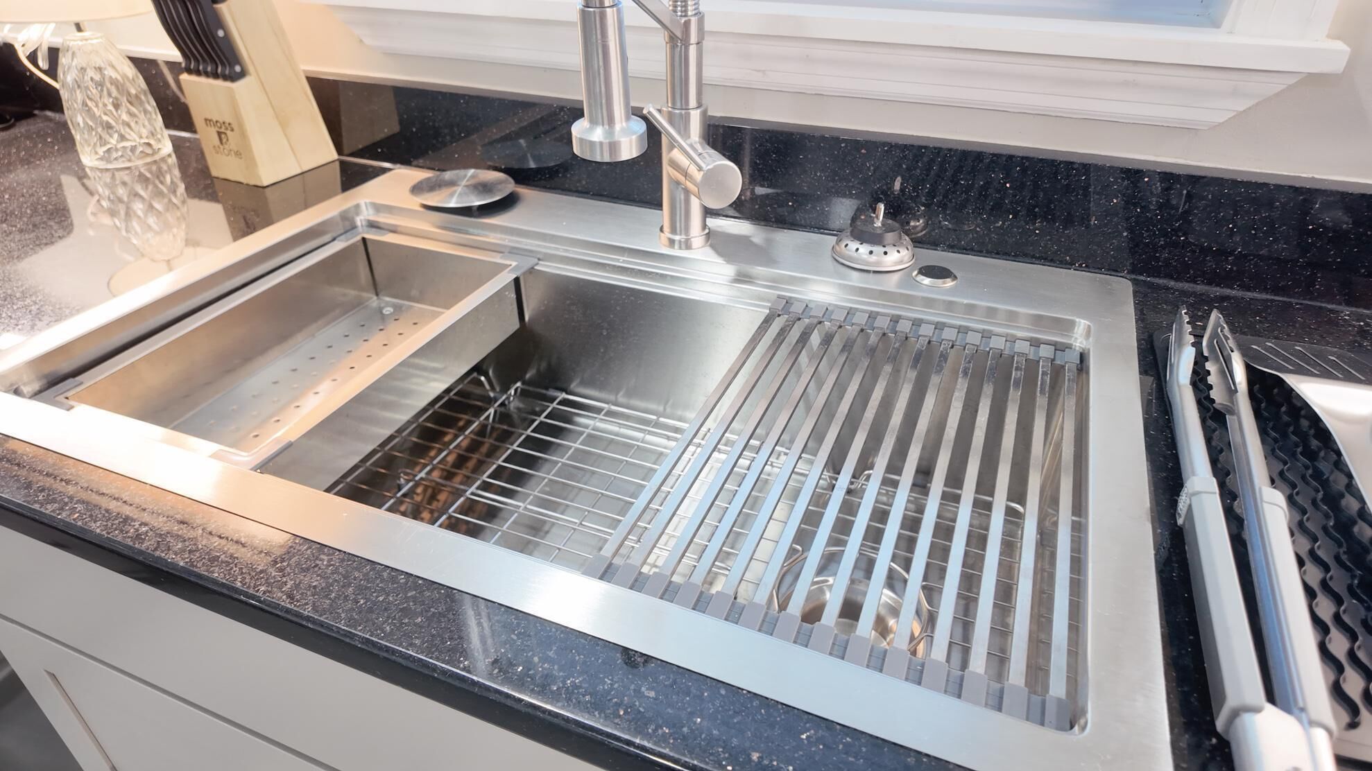 A stainless steel kitchen sink with a modern faucet, a dish rack, and a black granite countertop.