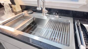 A stainless steel kitchen sink with a modern faucet, a dish rack, and a black granite countertop.