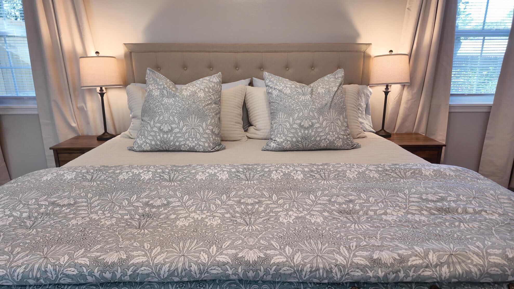 Una cama bien hecha con una colcha estampada de flores y dos almohadas a juego, flanqueada por mesitas de noche con lámparas.