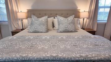 Una cama bien hecha con una colcha estampada de flores y dos almohadas a juego, flanqueada por mesitas de noche con lámparas.