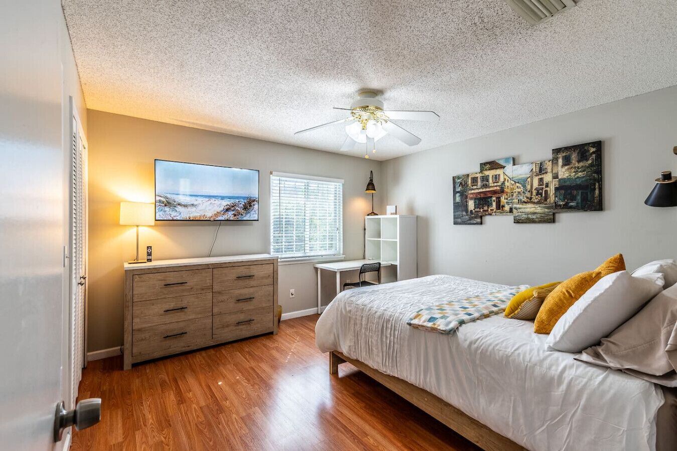 Ein Schlafzimmer mit Bett, Schreibtisch, Stuhl, Fernseher und Bildern an den Wänden.