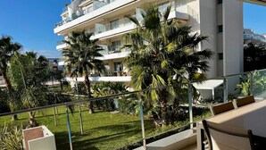 A balcony with a view of a multi-story building, palm trees, and a grassy area. - Marina Real in Denia (Denia)