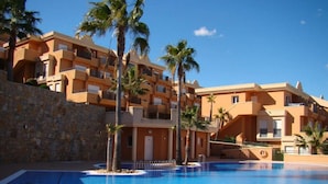 A swimming pool surrounded by a multi-story building with balconies, palm trees, and a stone wall. - Jacaranda in Pedreguer (Pedreguer)