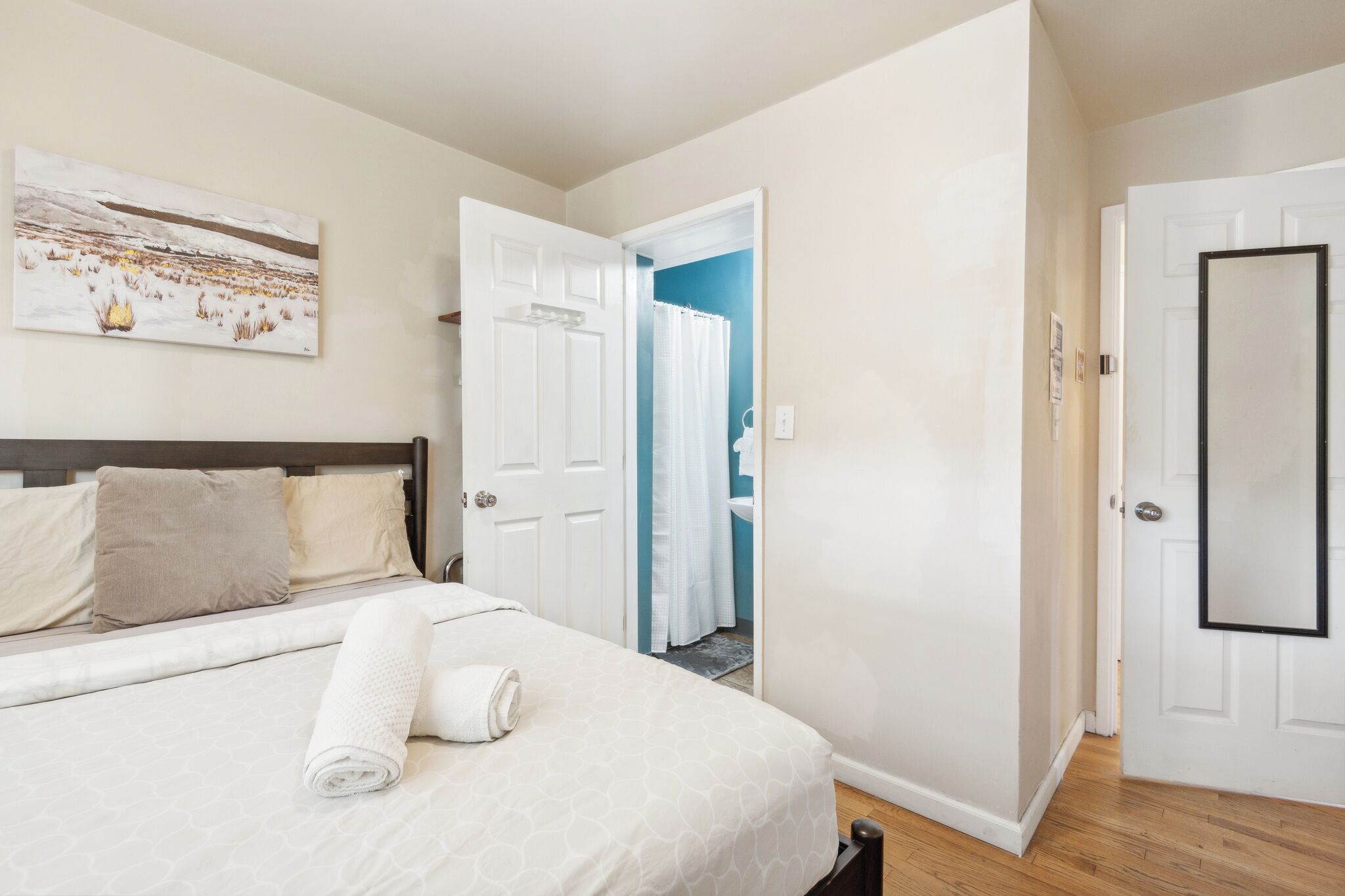 A bedroom with a bed, a painting on the wall, and a bathroom door.